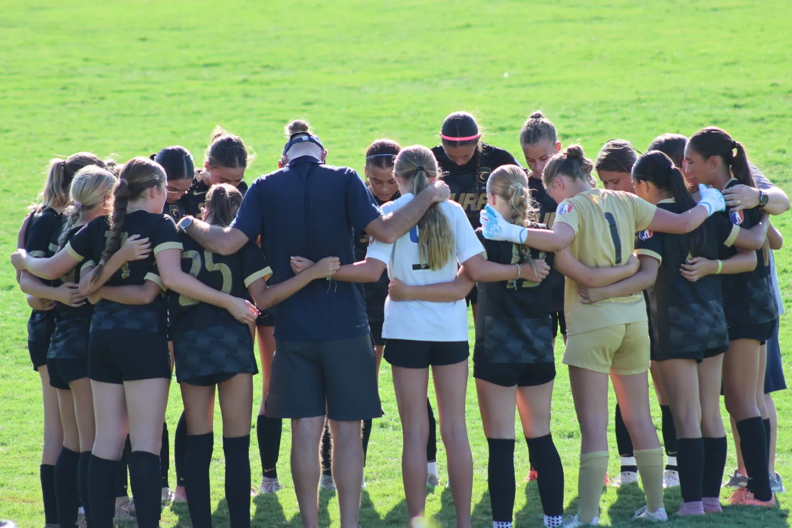 South Valley Surf girls arm in arm in a huddle circle on the field