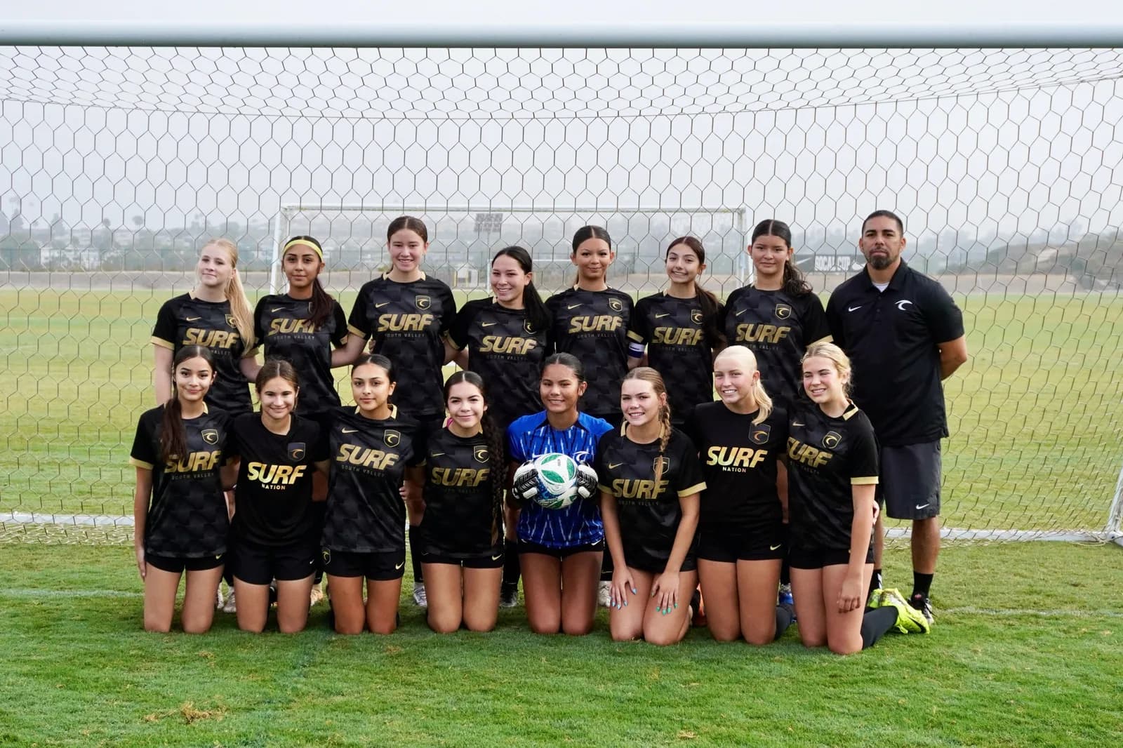 South Valley Surf girls team in black lined up with their coach in front of the goal